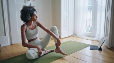 Pencere odasında bacaklarını açan zayıf bir kız. Kulaklıklı kadın lastik halıda meditasyon yaparken yoga dersi izliyor. Afrikalı sakin kadın gün ışığında vücudu ısıtıyor. Kıvırcık saç modeli evde egzersiz yapıyor.