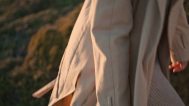 Closeup girl body going green hill in beige coat. Serene woman hiking evening landscape admiring nature at sunset. Beautiful curly female look camera enjoy weekend outdoors. Travel leisure concept