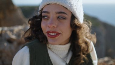 Closeup carefree tourist relaxing ocean cliff edge. Happy girl enjoy traveling admiring landscape with curls swaying in wind. Smiling woman traveler rest spring vacation. Serene peaceful mood concept.