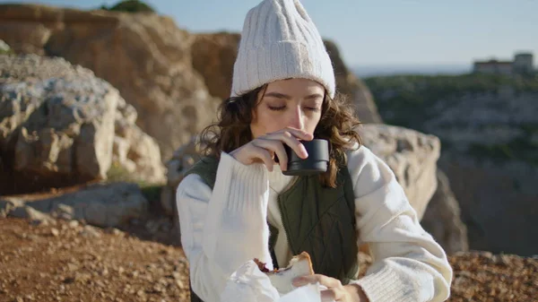 旅游女孩喜欢在岩石山顶吃饭 安静下来 闭目养神 在春日的阳光下喝咖啡 安静的女人在户外休息时吃点心 孤独生活平衡概念 — 图库照片