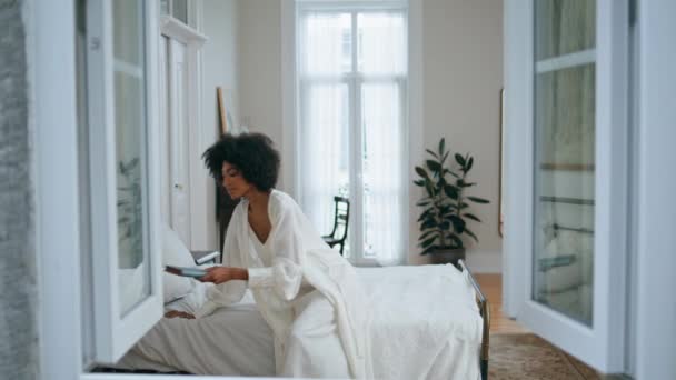 温文尔雅的女士在豪华卧室看书 黑发卷曲的女人在睡觉的地方白色的内部休息 迷人的非洲女孩喜欢在家里看故事书 一个人抱着最喜欢的小说的快乐模特 — 图库视频影像