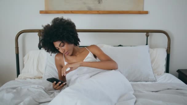把女士滚动手机放在卧室里在床上用智能手机冷静地检查社交媒体 放松女人在家上网聊天电话 性感的非洲女孩躺在枕头上 — 图库视频影像