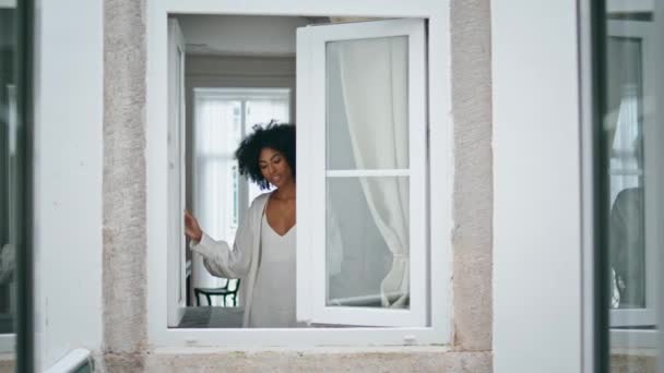 アフリカのモデルはリビングルームで窓を閉めた 黒い肌の幸せな女性の家で朝を過ごす 週末を楽しむリラックスした女の子 絹のガウンを着た夢の女性一人で休んでいる 家庭生活の概念 — ストック動画