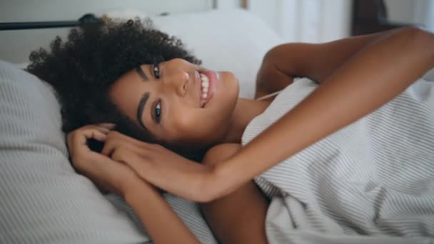 肖像笑脸模特躺在家里 卷发快乐的女人在早晨的卧室里看着相机醒来 非洲裔美国女孩在骨科床垫上小睡片刻后 享受着懒散的周末 — 图库视频影像