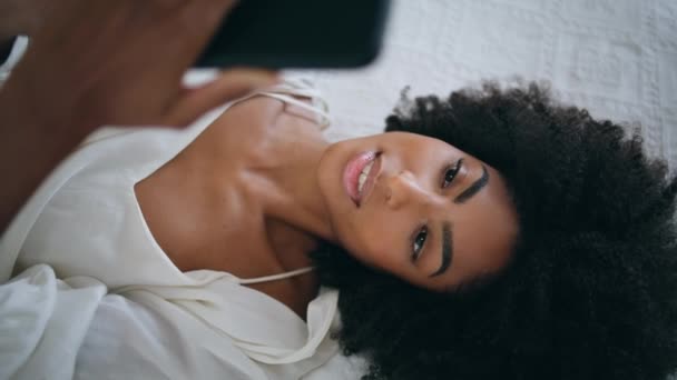 安静的女孩一个人躺在床上看留言 平静的非洲裔美国女士躺在卧室里 在家看智能手机电影 卷发模特在柔软的酒店床垫上放松 梦幻般的女人周末休息 — 图库视频影像