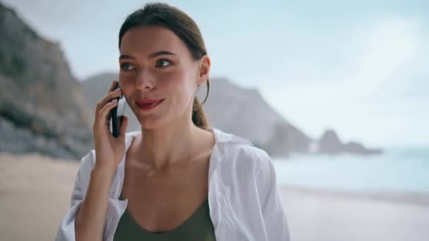 一个快乐的女人打电话给电话 独自走在多云的海滨的肖像 迷人的小女孩喜欢在暑假打电话聊天 在沙滩上讲智能手机的松懈女士关门了 — 图库视频影像