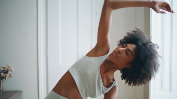 瑜伽女孩使斜坡关闭 田径女子在家里表演阿桑那 苗条身材的女士在早上的公寓里做着伸展侧角的姿势 非裔美国人运动教练在室内伸展身体 — 图库视频影像