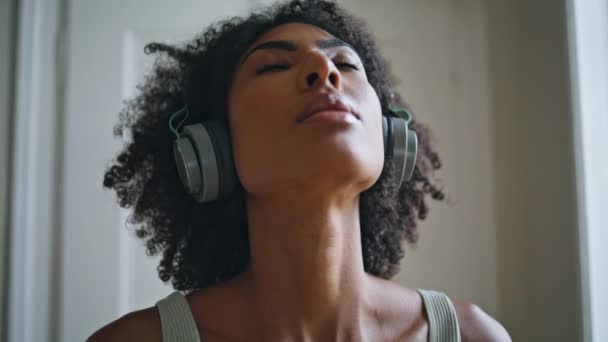 闭锁宁静的女人在室内深深地呼吸 非洲裔美国女运动员在家里闭着眼睛放松地独自面对着 吸引人的瑜伽女士在大耳机中进行吸入练习训练 — 图库视频影像