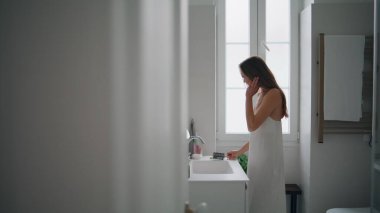 Young woman brushing hair in bathroom. Tender girl applying moisturizing mask after shower alone. Sensual lady looking mirror at morning apartment interior. Domestic beauty routine and care concept