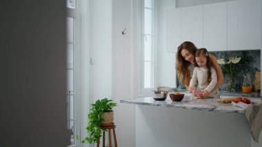 Cute family rolling dough out indoors. Loving mother daughter bonding together kneading pastry at kitchen. Adorable child helping to mom at home. Woman kid cooking at home interior. Traditions concept