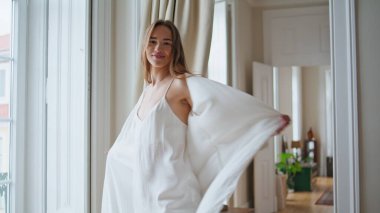 Happy woman dancing at light flat closeup. Smiling girl in silk robe spinning at luxury apartment. Positive lady spending morning at cozy home. Rejoicing female person looking camera having fun alone