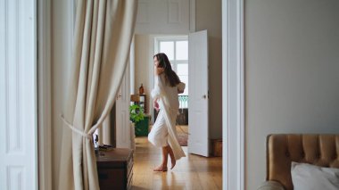 Dancing lady moving slowly at beige apartment. Lazy girl feeling joyful at light room. Happy woman in pyjamas enjoying weekends start at cozy home. Lovely female person welcoming new day alone at hall