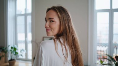 Flirting woman looking camera at home portrait. Smiling girl playing hair posing alone at beige apartment closeup. Sexy lady relaxing at morning house. Female person feeling joy resting at weekend