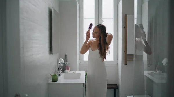 バスルームだけでヘアブラシを保持穏やかな女の子 現代のアパートで朝のヘアケアルーチンを行う自信のある女性 豪華な女性が鏡を家に立っている 国内のヘアスタイルコンセプト — ストック写真