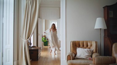 Carefree lady enjoying morning cozy interior. Tender woman feeling joyful having fun at light apartment. Positive girl dancing at beige home. Excited female person spinning with stretched arms alone