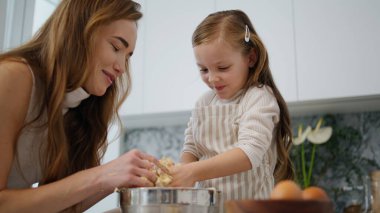 Mutfakta birlikte yemek pişiren güzel bir kız çocuğu. Yakın çekim. Aile evde kurabiye için hamur hazırlıyor. Genç anne çocuk modern iç mekanda pasta yapmaktan zevk alıyor. Annem pastayı çocuk ellerinden alıyor.