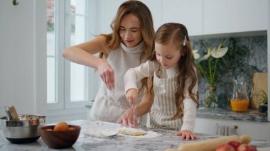 Cheerful woman pouring flour on table indoors closeup. Sweet family preparing food together. Mother and daughter time in kitchen room. Mom and child making biscuit at home. Homemade cuisine concept