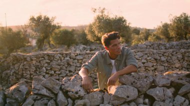 Gülümseyen model antik çitleri gevşetiyor. Sakin, bronzlaşmış bir adam yazın güneşli manzarayı seyrediyor. Olumlu yetişkin bir adam bahçe manzarasını seyrediyor sıcak ışıkta yalnız başına.