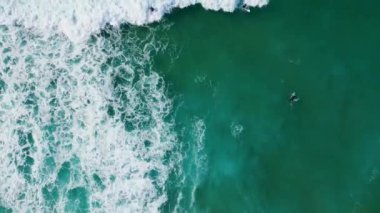 Sörf tahtasında okyanus dalgalarını bekleyen bilinmeyen sörfçüler. Extremal sörfçüler turkuvaz deniz yavaş çekimde kaykaydan hoşlanırlar. Köpüklü fırtınalı su tropikal sahilde süzülüyor.. 