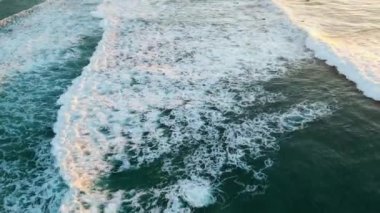 Drone manzaralı köpüklü deniz yazın gün batımında yavaş çekimde su sıçratıyor. Güzel mavi dalgalar kıyıya doğru yuvarlanıyor ve beyaz köpük yapıyor. Sersemletici deniz manzarası sakin okyanus sörfü deniz kenarını yıkıyor..