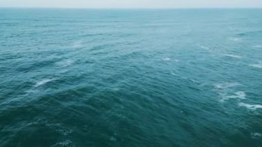 Panoramik hava manzaralı akşam deniz manzaralı sakin mavi okyanus suyu çok yavaş dalgalanır. Bulutlu gökyüzü altında deniz dalgaları. Yaz günü. Köpüren dalgalarla sakin, kasvetli deniz manzarası. Doğa yolculuğu.