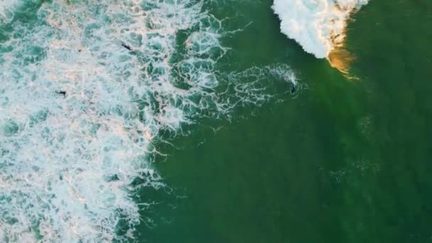 俯瞰泡沫般的海水流向海岸 溅出缓慢的水花 空降小组的冲浪者骑在波涛汹涌的浪尖上练习着极端的业余爱好 未知的人在夏日美丽的大海中冲浪 — 图库视频影像
