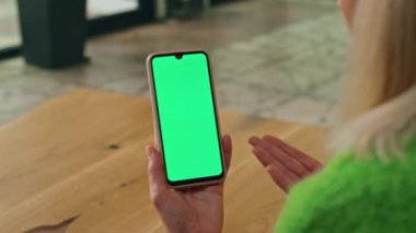 Kapalı alanda elinde yeşil ekran telefon tutan bir kadın. Ofisteki Chromakey akıllı telefonu arayan bilinmeyen bir çalışan videosu. Kadın yönetmen el hareketleriyle ekrandaki cep telefonu görüntüsünü yakınlaştırıyor.