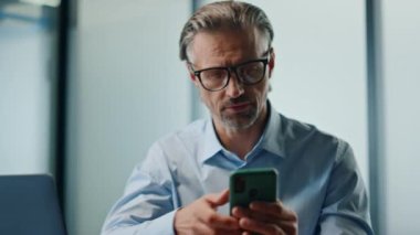 Ofis portresi üzerinde çalışan düşünceli bir adam. Akıllı telefon e-postası yazan odaklanmış işadamı dizüstü bilgisayardaki iş projesini kontrol ediyor. Gözlüklü patron modern işyerinde mobil çoklu görev yapıyor