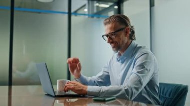 Aşırı sevinçli bir çalışan dizüstü bilgisayarını içeriden yakına çağırarak el sallıyor. İş yerindeki online bilgisayar görüntülü sohbette el kol hareketi yapan arkadaş canlısı bir adam. Resmi patron modern kabinede merhaba diyor. 