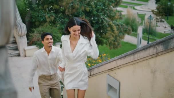 感情上的新婚夫妇在镇上跑楼梯 快乐的微笑的夫妻在城市景观外接吻 可爱的男孩拥抱在绿色的街道上 无忧无虑的Latina情人在户外共度浪漫的约会 — 图库视频影像