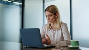 Ciddi bir iş kadını konferans odasından laptop 'ı arıyor. Odaklanmış girişimci, web kamerasıyla uzaktaki web sitesinde tek başına konuşuyor. Akıllı kadın internette video konferansında açıklıyor. 