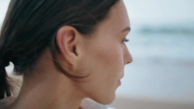 Nazik çekici kız modeli bulutlu bir günde poz veriyor. Yakın çekim. Dışarıdaki kameraya bakan güzel bir kadının portresi. Plajda doğal makyajlı sakin genç bir kadın yüzü. Güzellik konsepti.