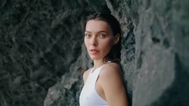ホット若い女の子のカメラ石の崖の屋外の近くに傾いている 岩の多い海岸に白い水着姿の魅力的なセクシー女性 海岸の山の近くに立つ美しい自信モデル — ストック動画