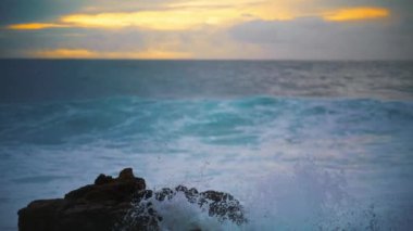 Okyanus sabahın erken saatlerinde kıyıdaki kayalara çarpıyor. Deniz kıyısında güzel bir akşam sörfü. Ağır çekimde deniz kıyısına çarpıyor. Sersemletici bulutlu manzarada köpüklü su. Güneş doğmadan önce gevşetici deniz manzarası