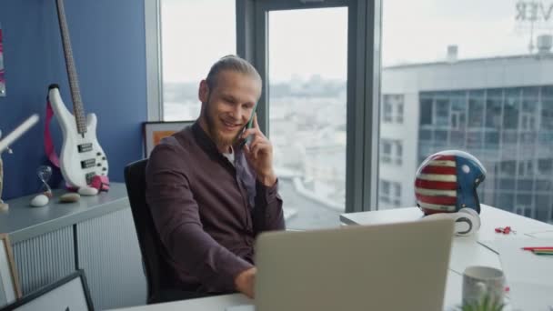 快乐的自由职业者打电话给总部的手机特写 笑着看电脑屏幕上的程序员在屋里讨论电话 英俊的男人一个人在嬉皮士公寓工作技术概念 — 图库视频影像