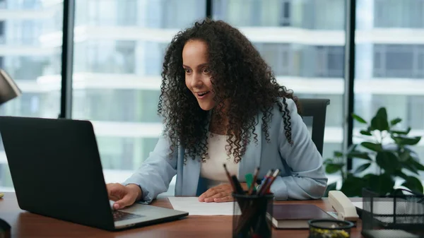 Happy woman surprised company financial results reading report on laptop close up. Portrait of latin curly businesswoman satisfied business achievement. Brunette girl smiling working in modern office.