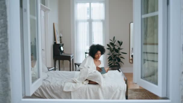 无忧无虑的女人翻书 非洲裔美国人轻松地阅读小说铺床 积极的卷曲模型 在卧室内部与文学一起放松 教育休息生活方式概念 — 图库视频影像