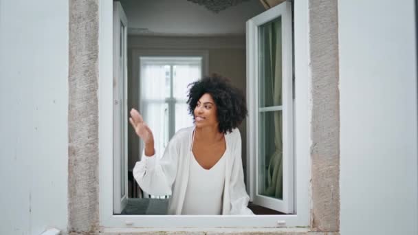 一个黑头发的姑娘在早晨的房子里摇着窗户 蜷曲的微笑着的女人看着外面的天气 快乐的非洲裔美国人模式观看城市景观享受在家里的梦想 日常概念 — 图库视频影像