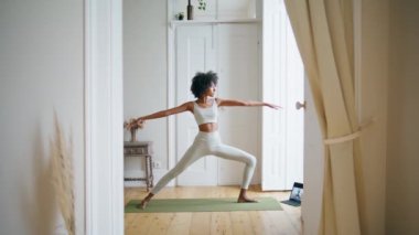 Evde yoga yapan sakin bir bayan. Afro-Amerikan rahat kız ayakta poz veriyor. Beyaz iç kısımda zayıf sporcu kadın uzanıyor. Spor eğitmeni sadece kenar açı duruşunu genişletiyor. 