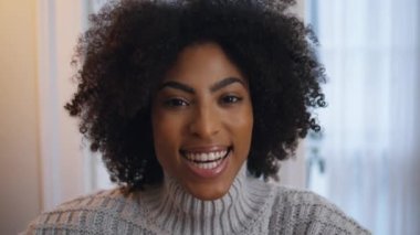 Mutlu kız gülümseyen kamera akşam ev portresi. Kaygısız, duygusal bir kadın rahat bir yerde oturuyor ve yalnız başına yakından bakıyor. Afrikalı makyajcı kadın düz objektife bakıyor. Pozitif model pozu