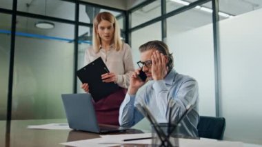 Sinirli iş adamı ofisteki akıllı telefondan bahsediyor. Dizüstü bilgisayarda çalışan stresli çift. Sinirli adam telefonda konuşuyor. Tatmin olmamış iş yakın plan. Endişeli kadın karışık konuşuyor.