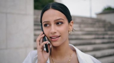 Kapalı çekim gülümseyen kız merdiven boşluğunda telefonla konuşuyor. Sokakta iletişim kuran akıllı telefon kullanan mutlu Latin kadın. Mimarinin dış cephesinde telefon bekleyen rahat iş kadını konuşuyor.