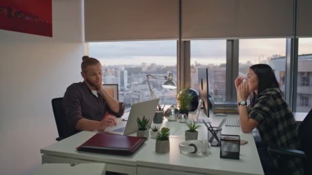 疲れて同僚のオフィスの日没作業 現代の職場でコンピュータを見て疲れ果てた人々 ビジネスカップルは プロジェクトの締め切り都市ビューウィンドウの夜のオープンスペースを一緒に座って — ストック動画