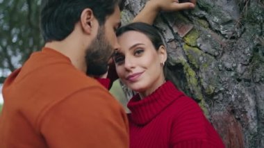 Geniş bir ağacın yakınında genç bir çift poz veriyor. Çekici, rahat, kameraya bakan, erkek arkadaş sarılması. Güzel bir çift parkta romantik bir hafta sonunun tadını çıkarır. Boş zaman konsepti