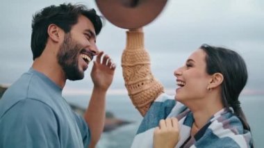 Mutlu mutlu çift sahilde sana sarılıp eğleniyor. Gülümseyen olumlu aile çifti gri okyanusun önünde durmuş birlikte hafta sonunun keyfini çıkarıyorlar. Şapkalı çekici genç kadın, sakallı adama sarılıyor..