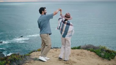 Bulutlu, sakin okyanus manzarasına karşı dans eden mutlu çift. Sevimli sakallı adam, şapkalı çekici kadını kaldırıyor. Gülümseyen sevimli turistler deniz kıyısında romantik bir hafta sonunun keyfini çıkarıyorlar. Aile çiftleri doğada rahatlar.