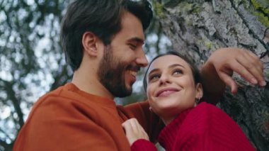 Romantik yakışıklı adam, geniş orman ağacına yaslanmış mutlu kadına sarılıyor. Sevgi dolu genç bir çift gülerek sonbahar doğasında hafta sonunun tadını çıkarır. Neşeli, sevecen aile çifti dışarıda keyif çatıyor..