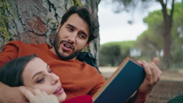 一个英俊的大胡子男人在野餐时看书 为放松的女人拉近距离 迷人而沉着的女孩躺在男朋友胸前享受周末的自然生活 可爱的浪漫夫妇一起在公园度假 — 图库视频影像