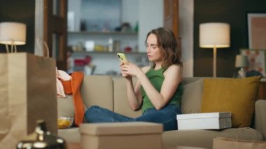 Evde koltukta oturan cep telefonu daktilo eden odaklanmış bir kız. Alışveriş bağımlısı bir kadın, dağınık bir kanepede elinde telefonla kıyafet sipariş ediyor. Oturma odasında tek başına akıllı telefonuyla sevinen neşeli bayan.