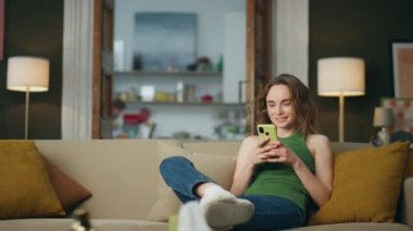 Gülümseyen kız evde cep telefonuyla konuşuyor. Cep telefonu tutan olumlu bir kadın sosyal medyada ev ortamında geziniyor. Oturarak mesaj okuyan rahat bir kadın. Akıllı telefon ekranına bakan kız 